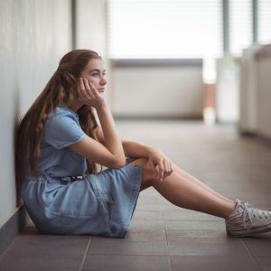 Sad schoolgirl sitting in corridor of school