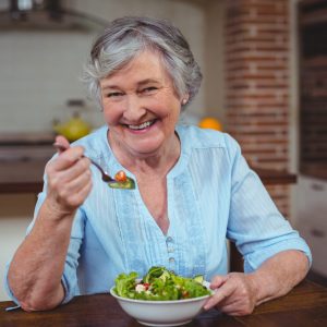 Portrait of smiling senior woman having vegetable salad in kitchen