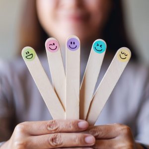 A woman holding colorful hand draw happy emotion faces on wooden stick