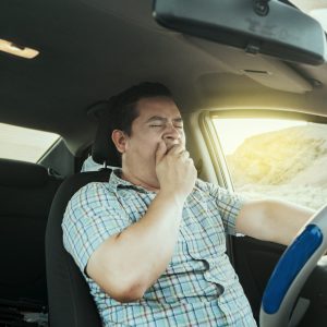 View of a sleepy driver in his car. Tired driver yawning in the car, concept of man yawning while driving. A sleepy driver at the wheel, a tired person while driving